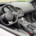 Interior of a car cabin showing a black steering wheel with an Audi logo, dashboard gauges, and a central console with a gear shifter and navigation screen