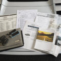 Set of Audi vehicle documents, brochures, and key fobs spread on the hood of a silver car, including warranty and service papers.