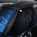 Open sports car interior with a black racing bucket seat and Willans harness, windshield reflecting the sky.